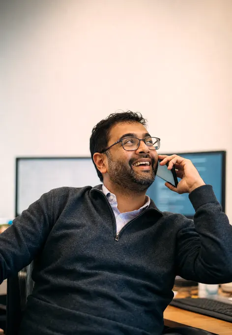 A university IT director leaning back at his desk mid-call, grinning at something the caller said
