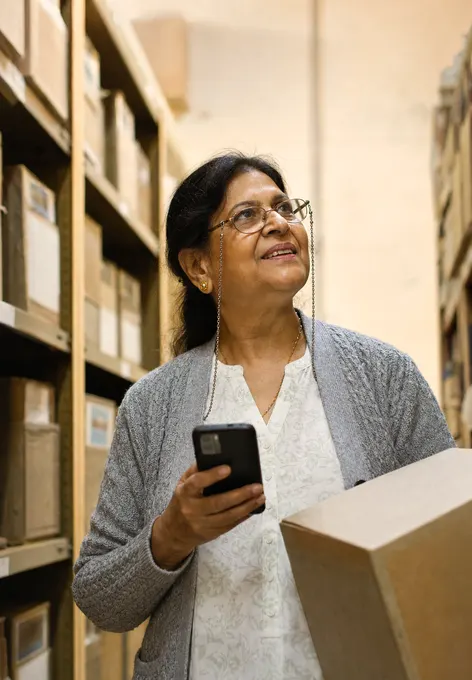 A records officer between archive shelves holding a box, looking up as if she just found the file