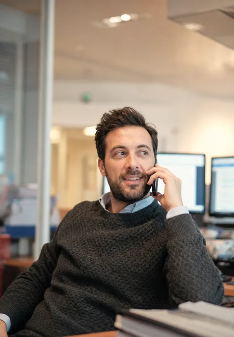 A revenue-cycle analyst leaning back at his desk, mid-call on his phone