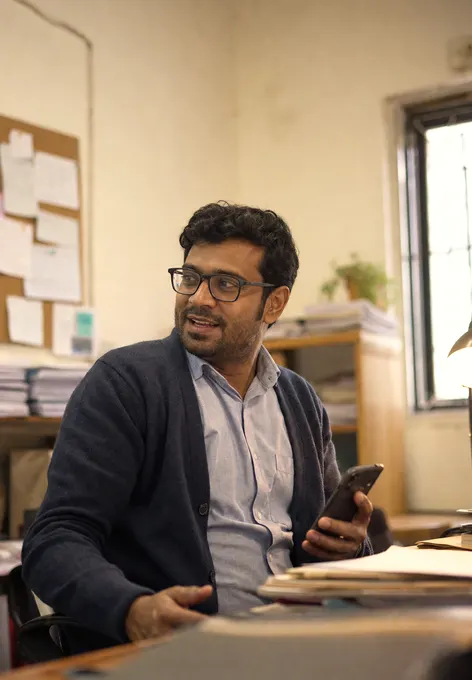 A grants manager at a cluttered desk turning to talk to someone off frame, phone in hand